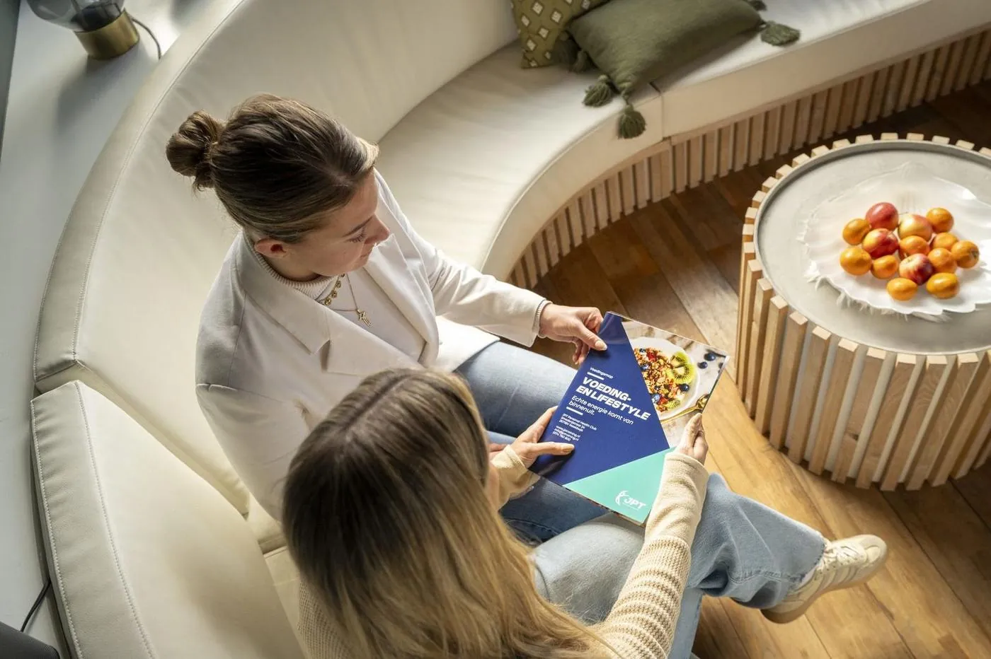 Intakegesprek tussen coach en nieuwe cliënt in lounge stoelen, van bovenaf gezien